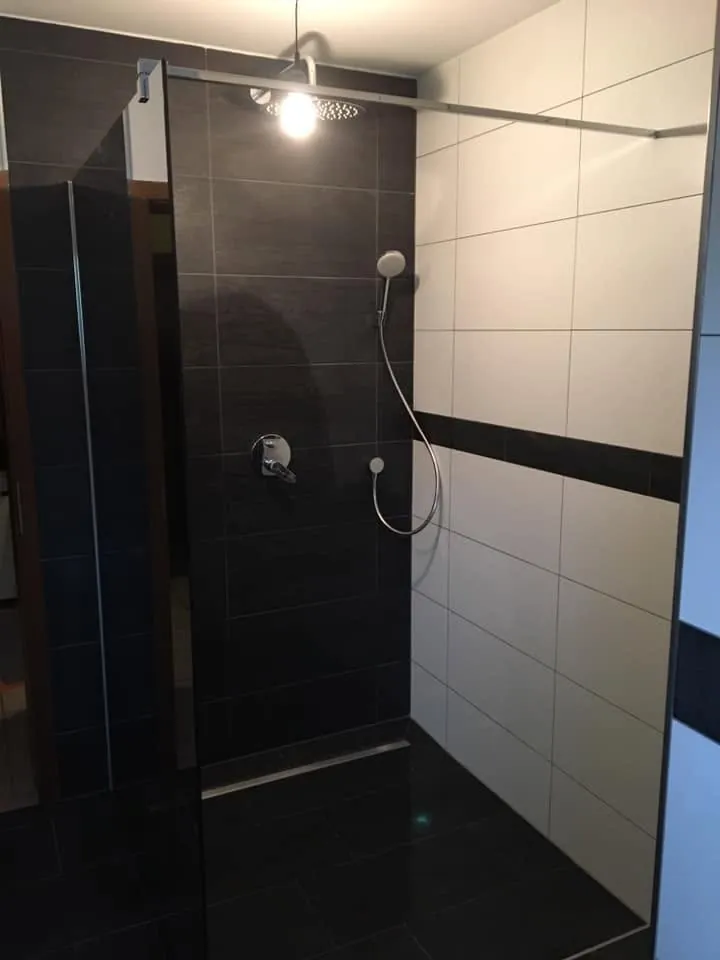Bodengleiche Dusche mit dunklen Wandfliesen und hellem Fliesenband