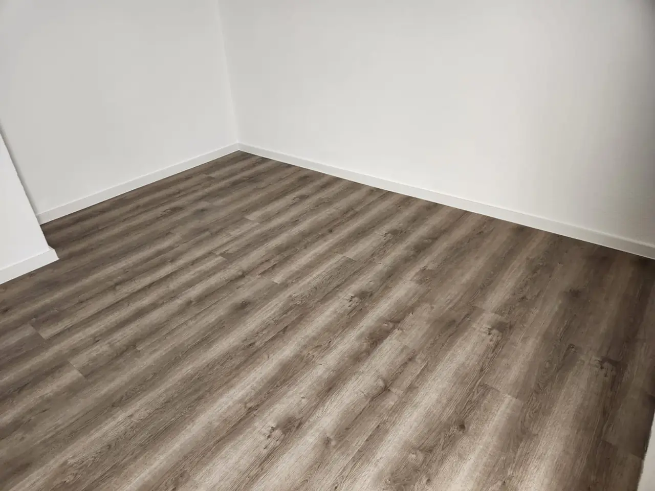 Fertig ausgebauter Raum mit Bodenbelag in Holzoptik, weißen Wänden und Sockelleisten