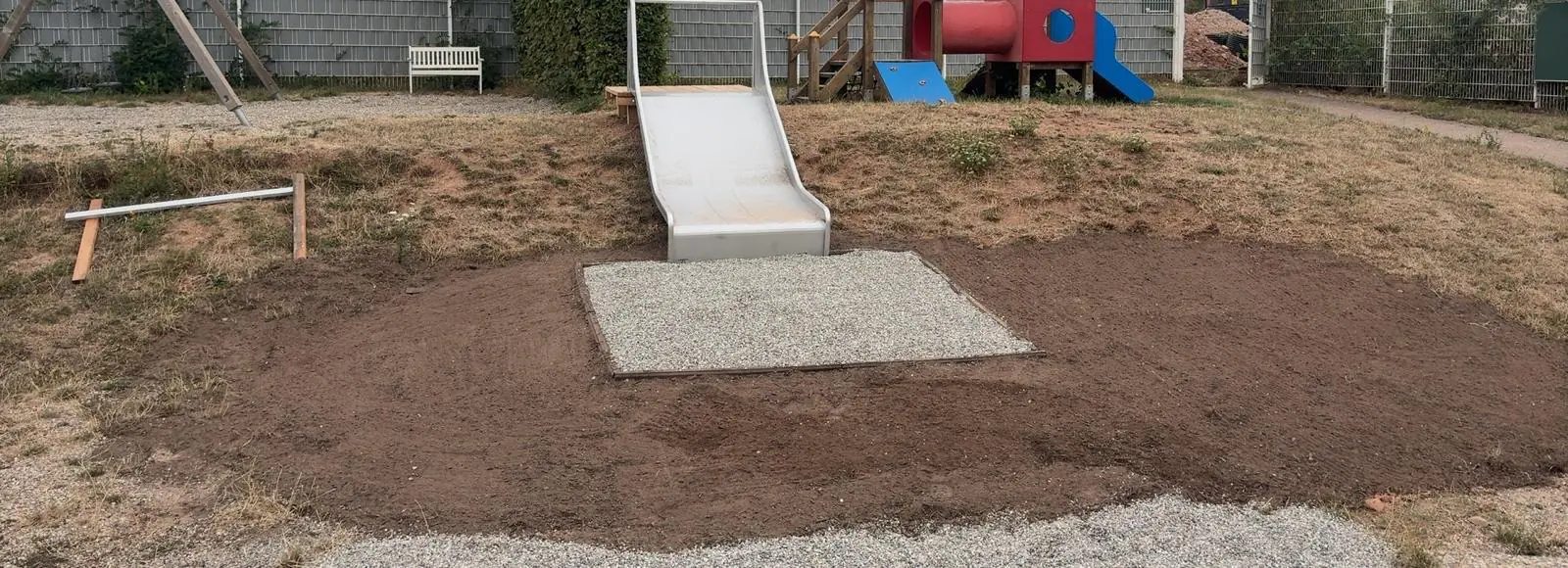 Erdhügel mit eingebauter Rutsche vor dem Spielturm der Kita
