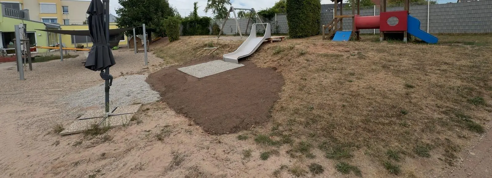Blick über das Spielgelände der Kita mit Rutschenhügel und Sonnenschirm